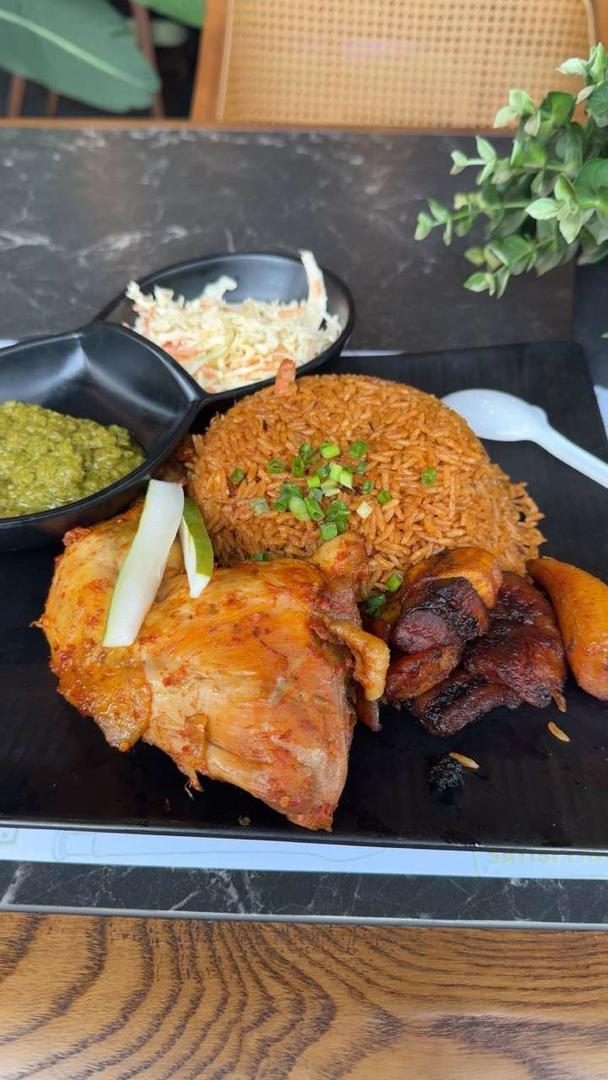 A plate of authentic Ghana jollof rice with grilled chicken, fried plantain, coleslaw and green pepper sauce