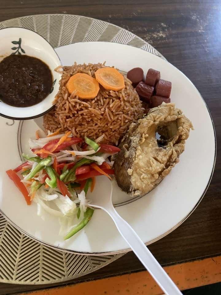 Ghana jollof rice served with whole fried fish, fresh salad and dark shito pepper sauce